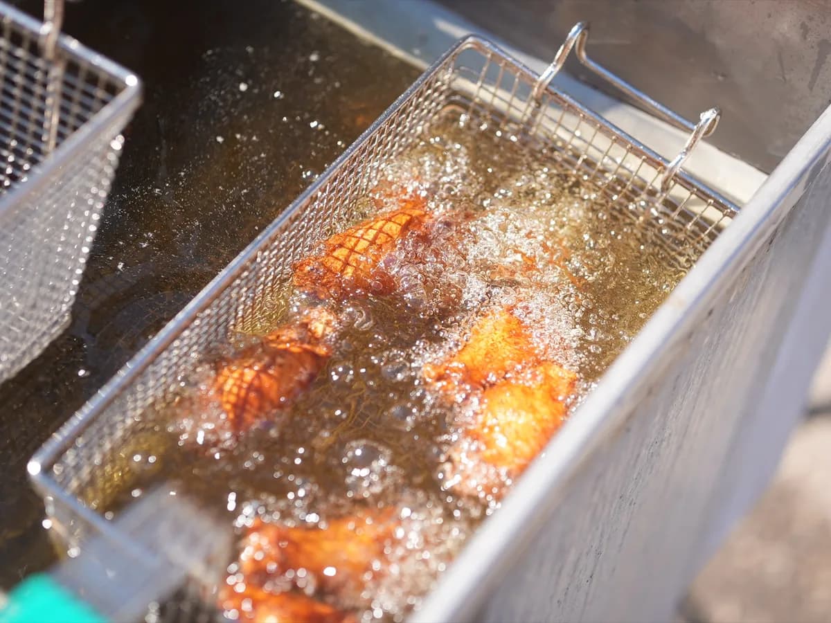 Chicken wings frying in bubbling oil in a basket, cooked to order on site at the festival